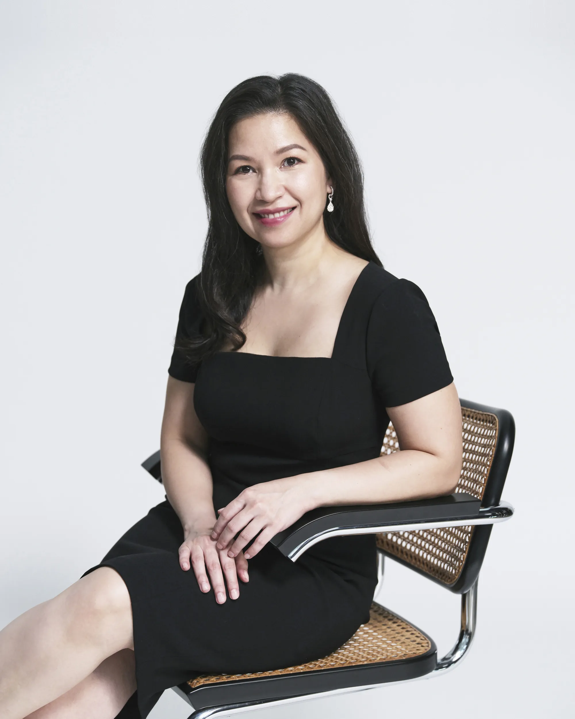 Dr Chang Fu Shi, seated in a cane chair in a black dress, smiling at the camera